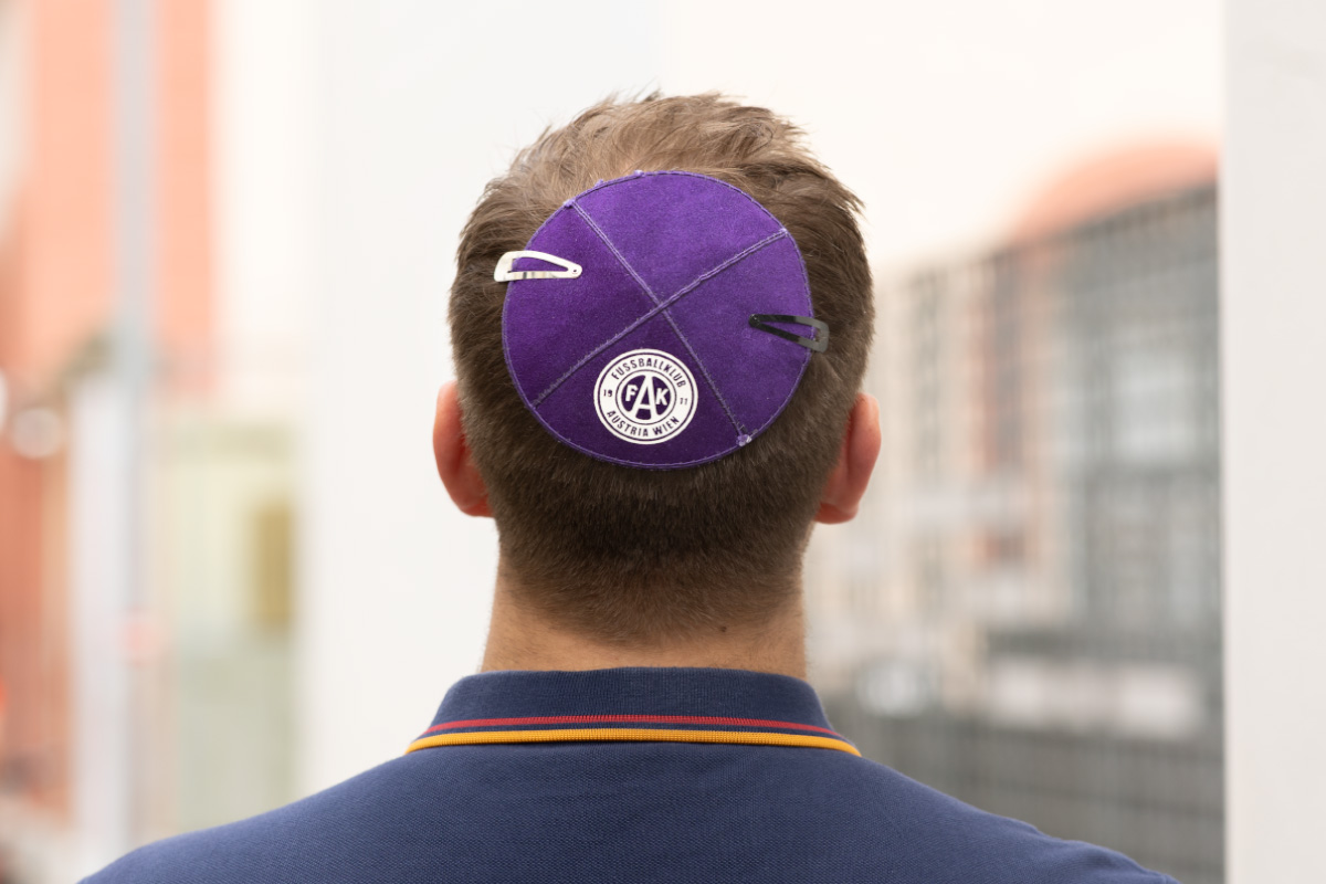 Mann von hinten mit einer violetten Kippa mit dem Logo des FK Austria Wien, festgehalten mit zwei Haarspangen