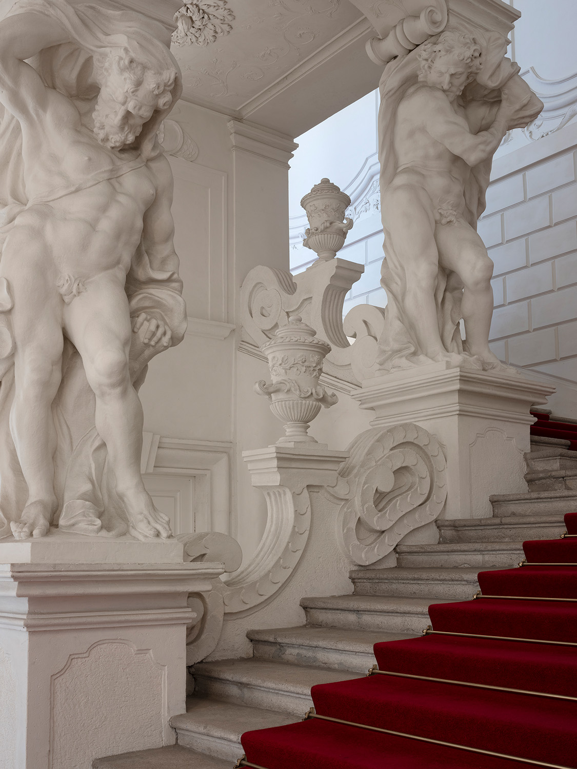 Stiegenaufgang mit marmornen Atlanten und einer mit rotem Teppich ausgelegten Treppen