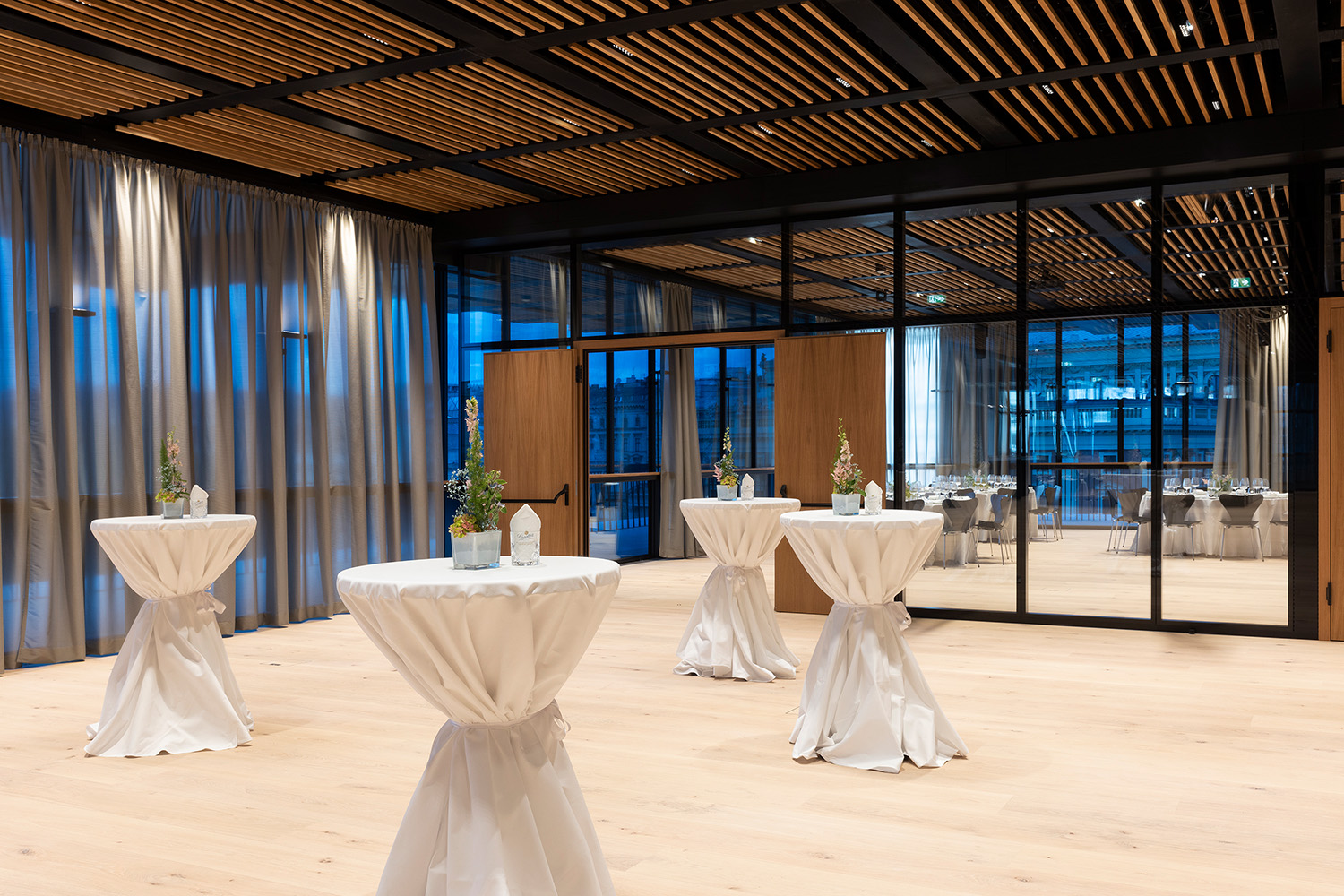 Freiraum mit Stehtischen und Blumen, Blick auf Saal mit Tischen für ein Galadinner