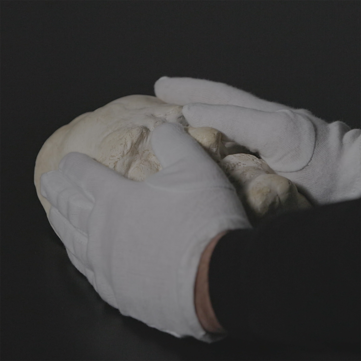Totenmaske wird von zwei Händne mit weißen Handschuhen umfasst