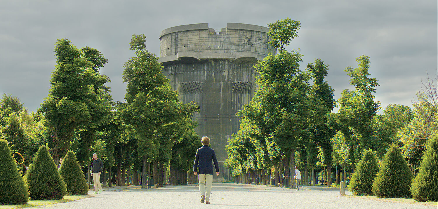 Mann geht zwischen Bäumen auf einen Flakturm zu