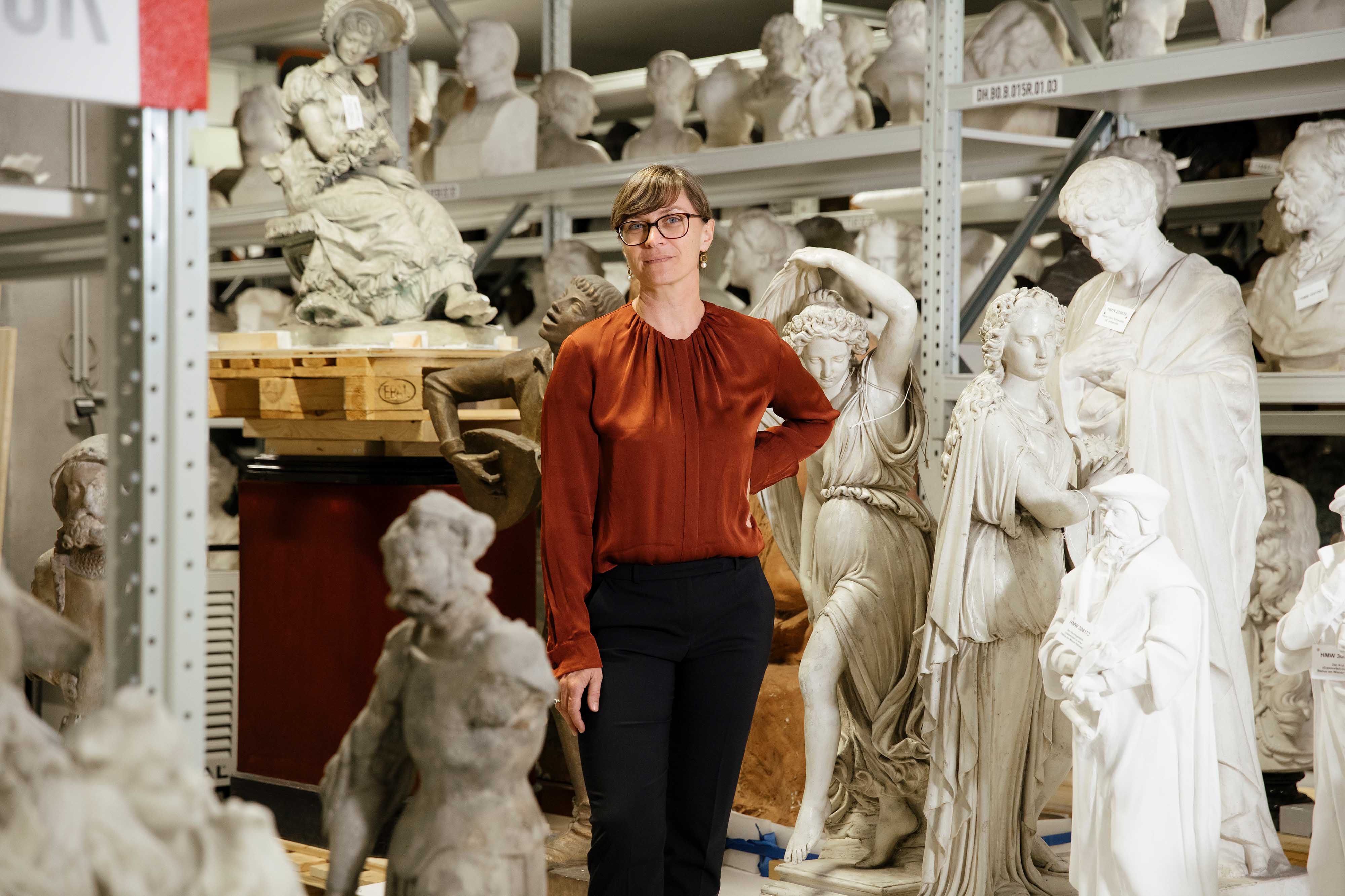 Frau im Sammlungsdepot des Wien Museums umgeben von mehreren Statuen.