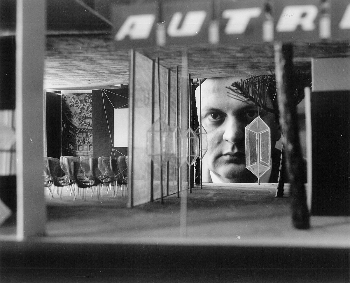 Schwarz-Weiß-Fotografie eines Ausstellungsraums mit Sitzgelegenheiten und modernen Dekorelementen. Im Hintergrund ist ein großformatiges Porträt Karl Schwanzers zu sehen.