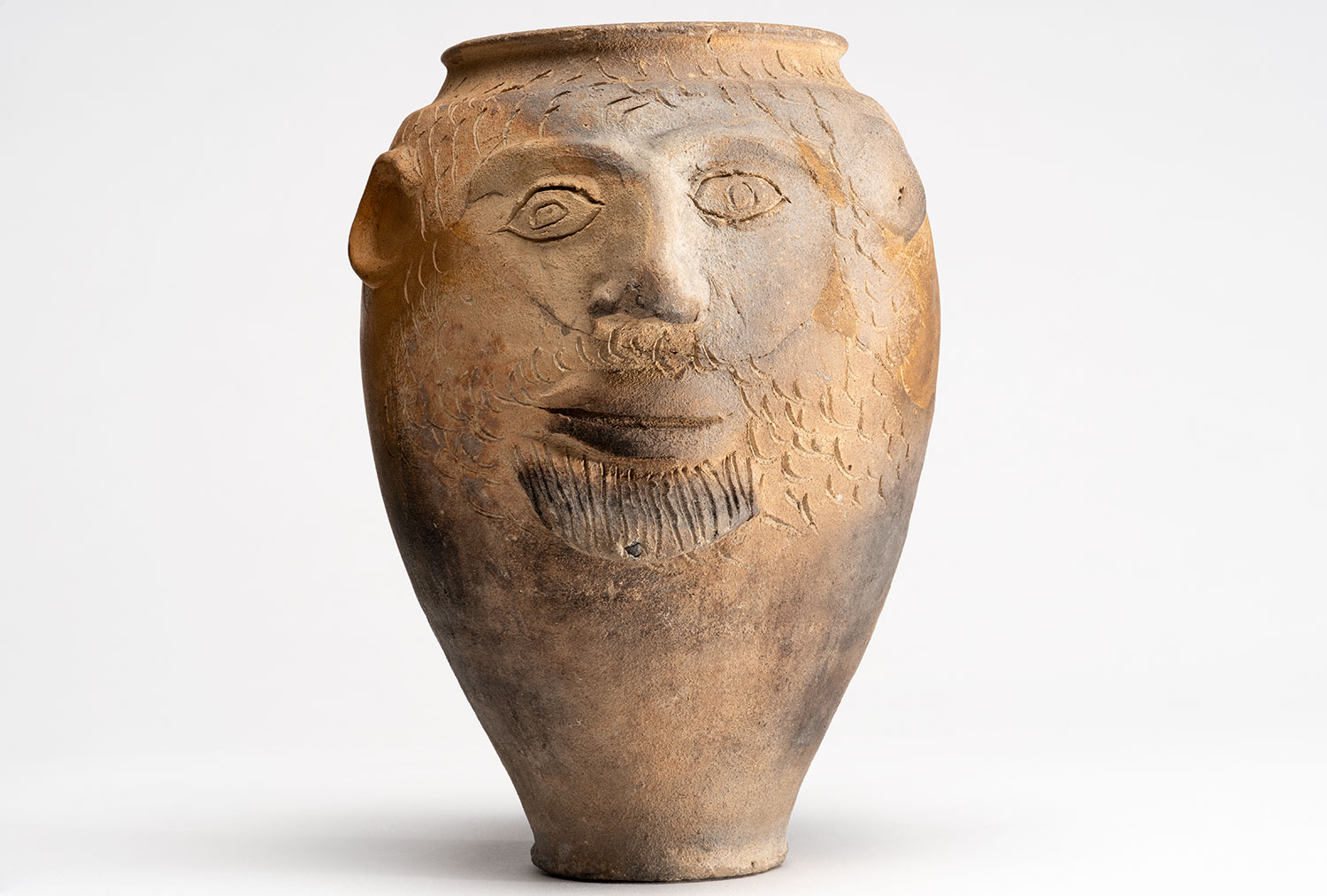 Eine braune Vase mit einem Gesicht und Ritzungen für Haare und Bart. Links ein gut sichtbares Ohr 