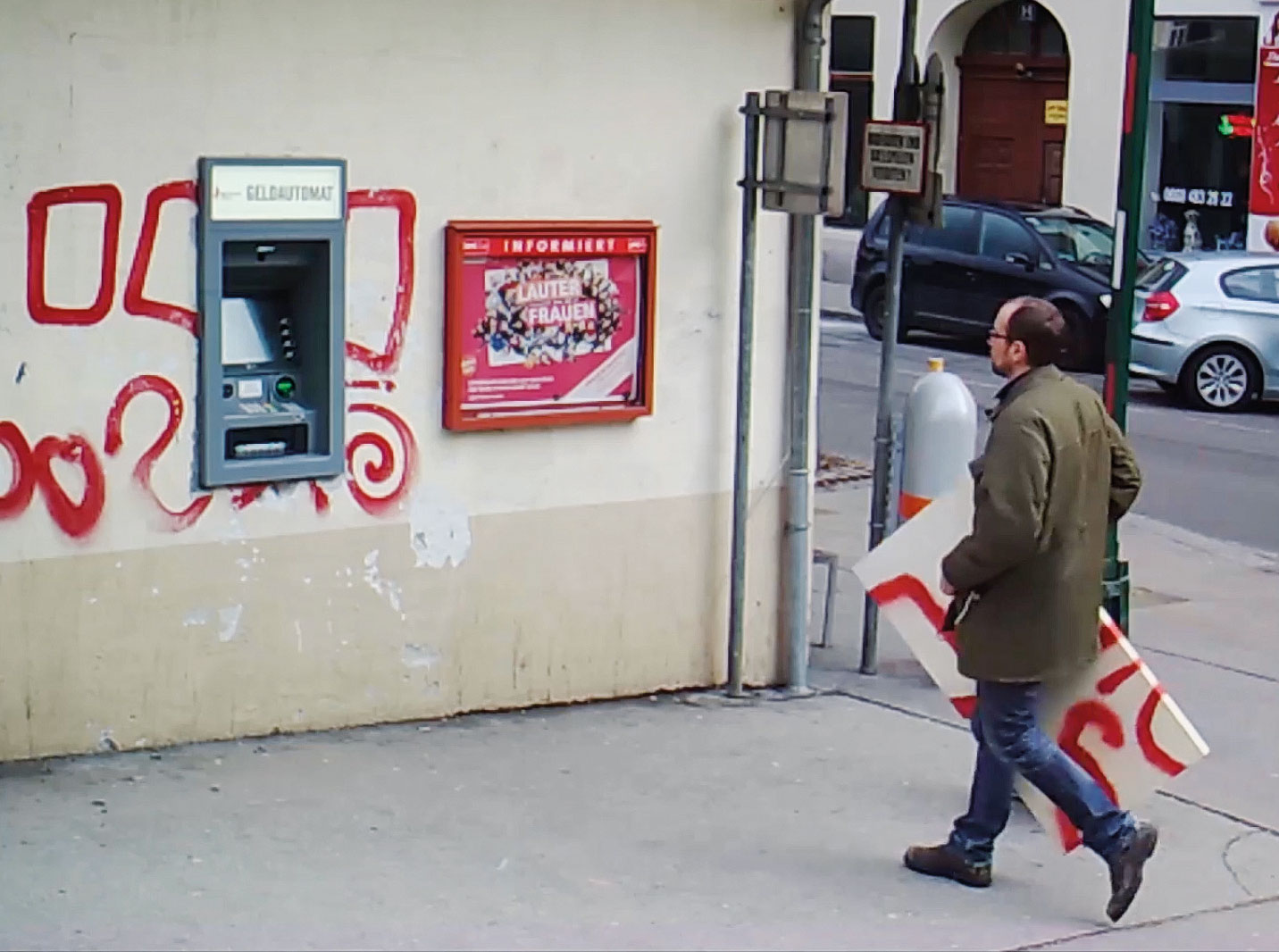 Mann geht mit einem bemalten Bild auf einen Bankomat in der Mauer eines Hauses zu