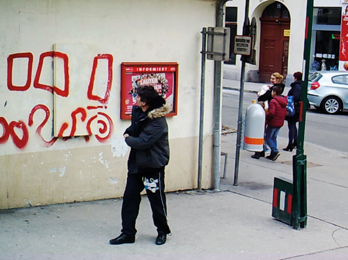 Mann sieht auf die Mauer eines Hauses mit einem unter einem Bild mit Graffiti verdeckten Bakomaten