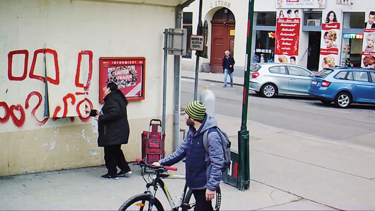 Die Frau hebt das Bild an der Mauer an, um den sich dahinter befindlichen Bankomaten zu erreichen.