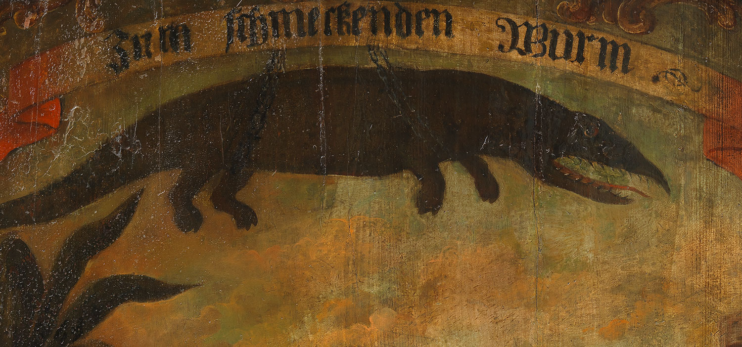 Oben befindet sich die Inschrift „Zum schmeckenden Wurm“, darunter ist ein krokodilähnliches Tier zu sehen.