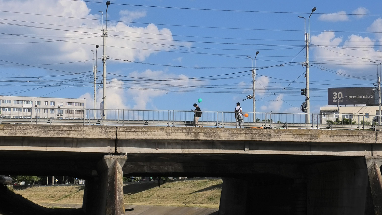 Auf einer Brücke gehen zwei Männer mit einem farbigen Ballon an einander vorbei