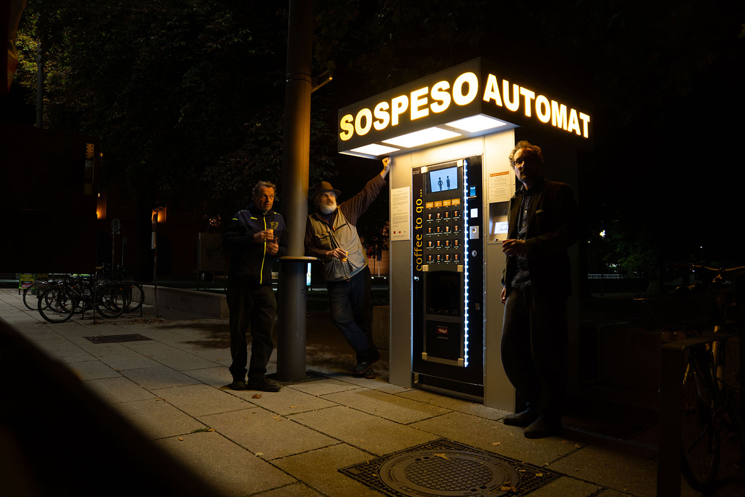 Männer stehen im Dunklen um den beleuchteten Kaffeeautomaten 