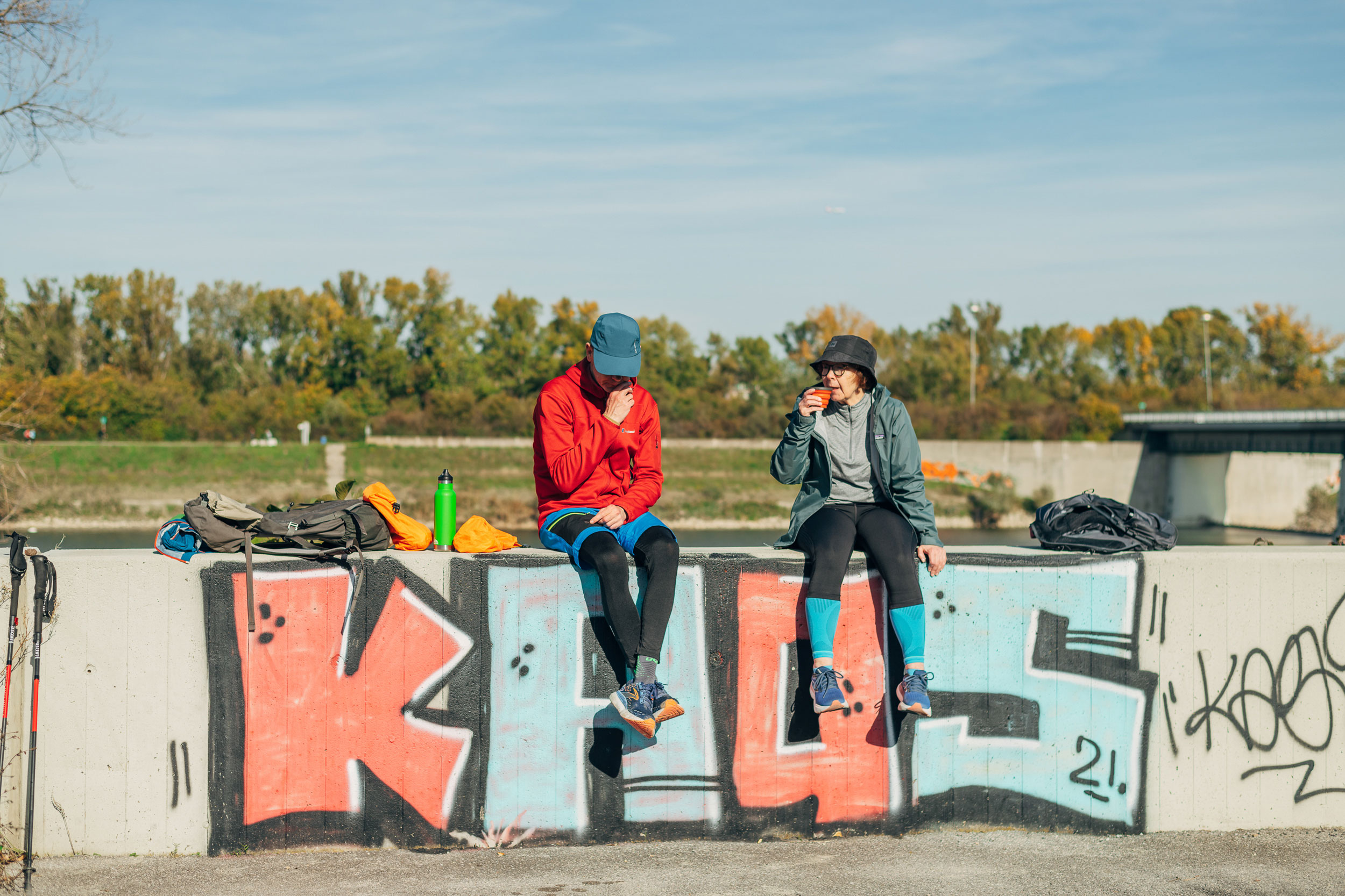Zwei Menschen sitzen auf einer Wand mit Graffiti und genießen die Sonne.
