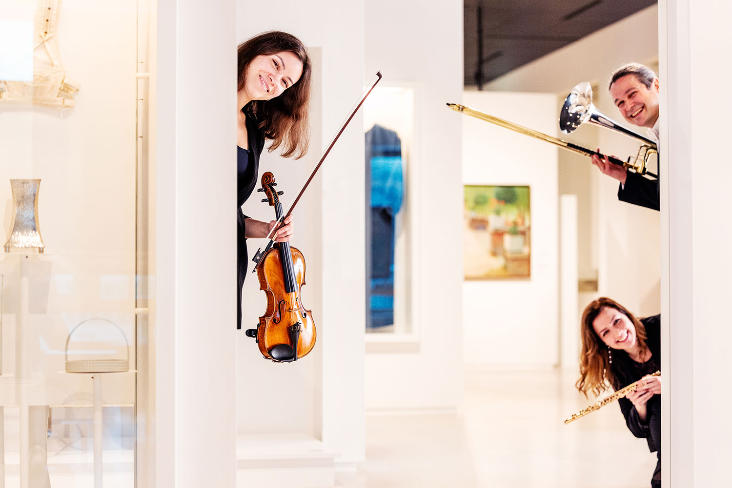 Drei Musiker:innen stehen in der Daueraustellung mit ihren Instrumenten und schauen zwischen Stelen in die Kamera