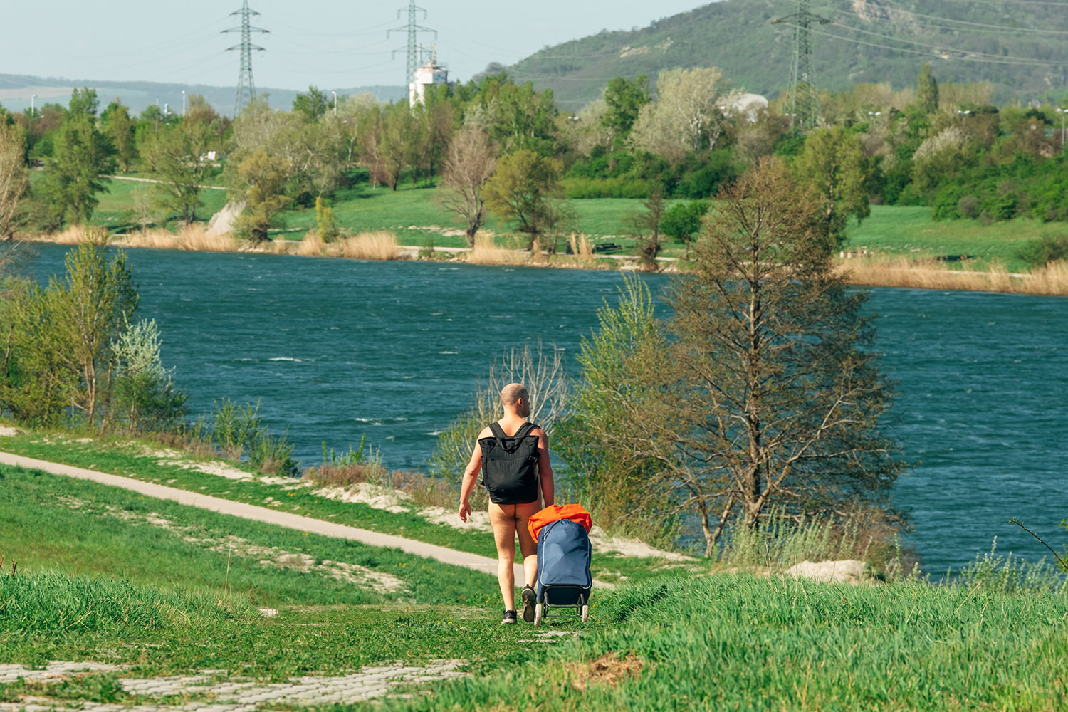 Nackter Mann von Hinten mit Rucksack und Trolley
