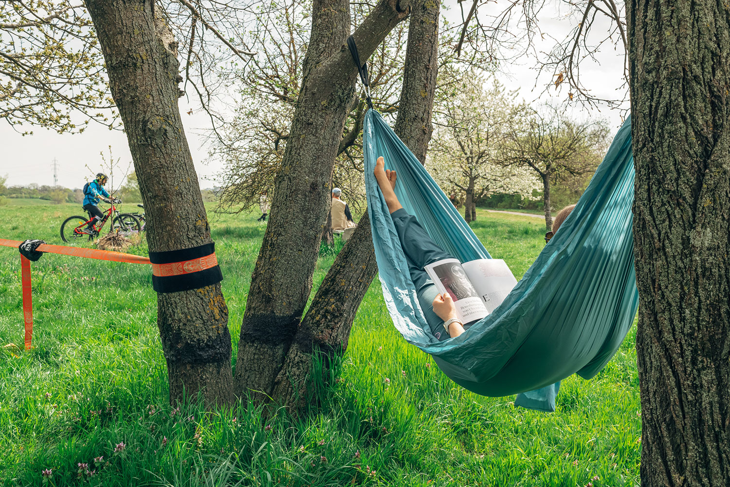 Lesende Person in einer Hängematte, im Hintergrund ein Radfahrer