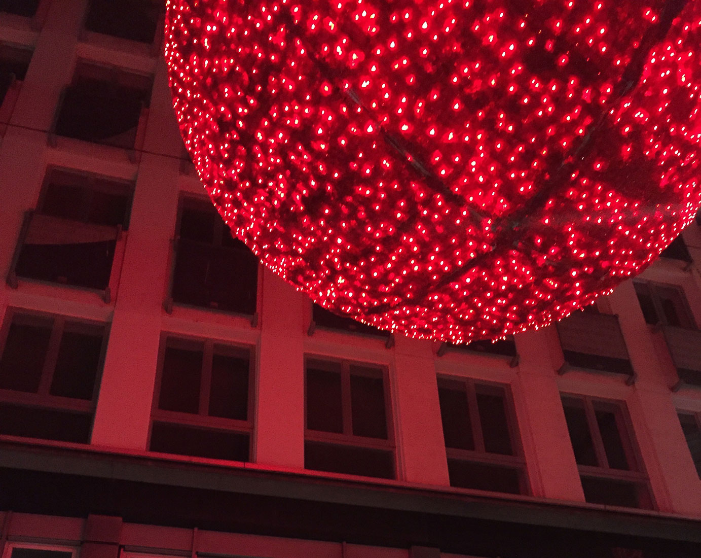 Große, rote und beleuchtete Weihnachtskugel der Straßenbeleuchtung spiegelt sich auchg im Fenster eines Hauses 