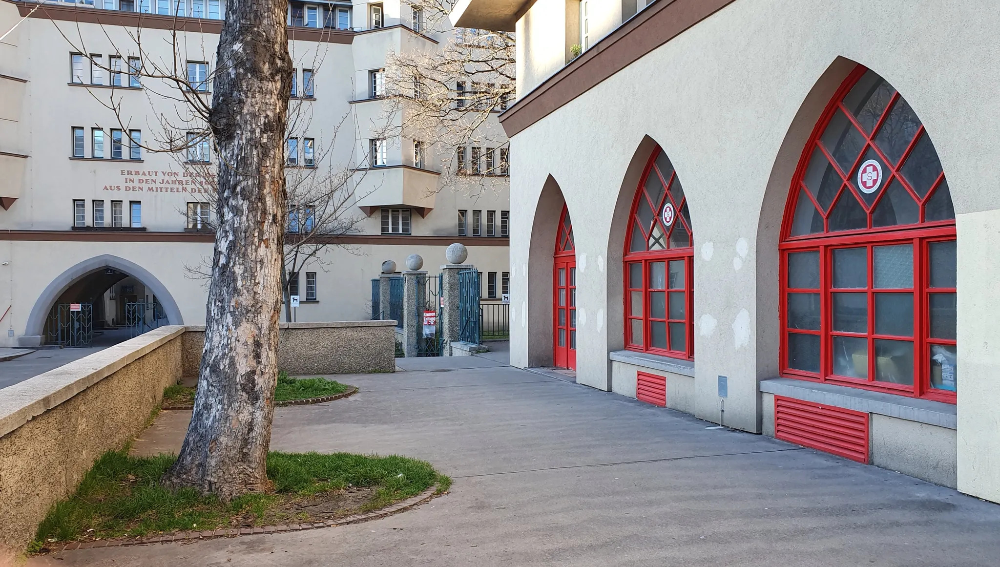 Fassade des Gebäudes mit roten Fensterrahmen und Baum davor 