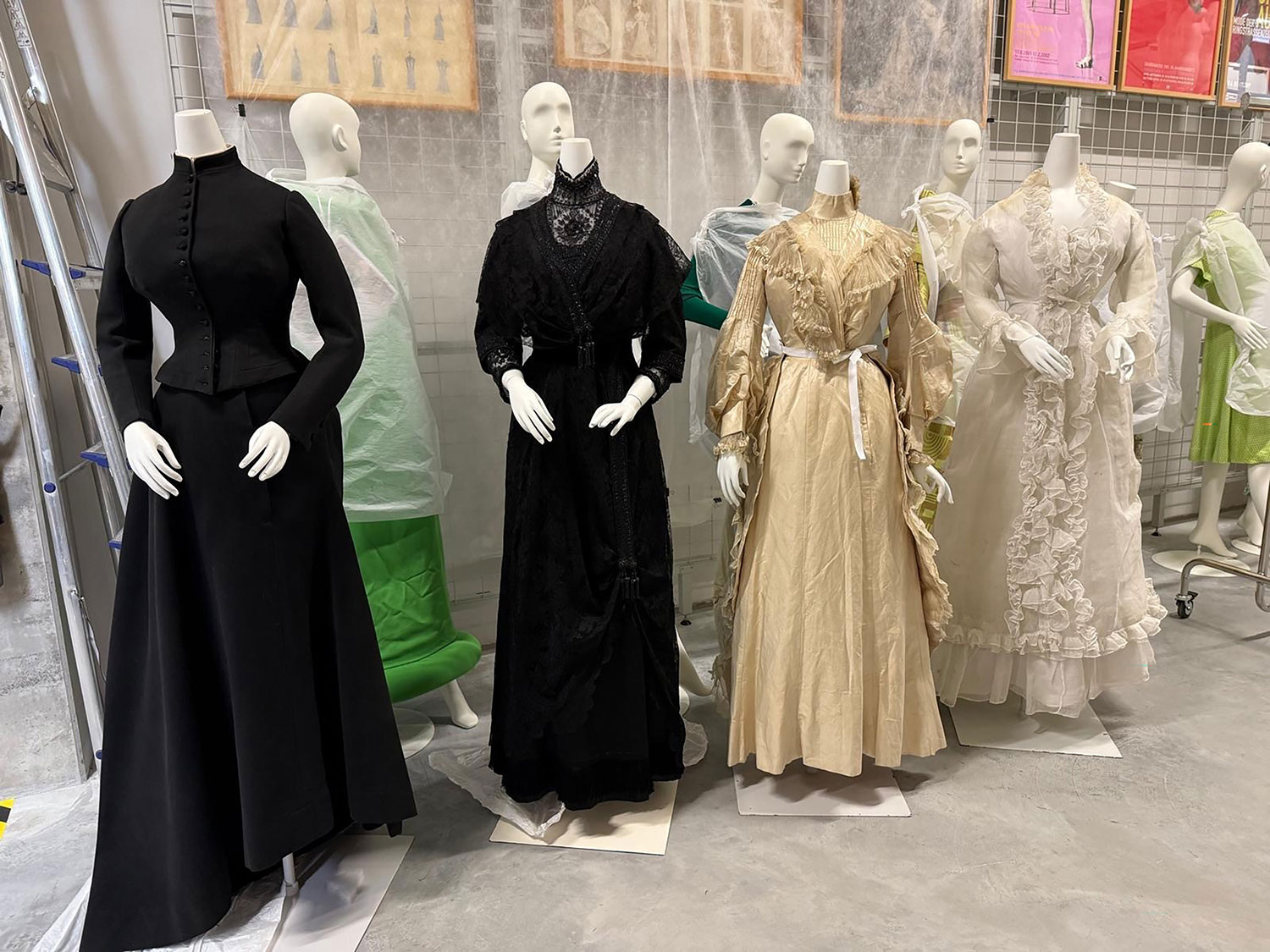 Kleiderpuppen mit Kleidern in verschiedenen Farben – schwarz, beige und weiß – mit unterschiedlichen Schnitten. 