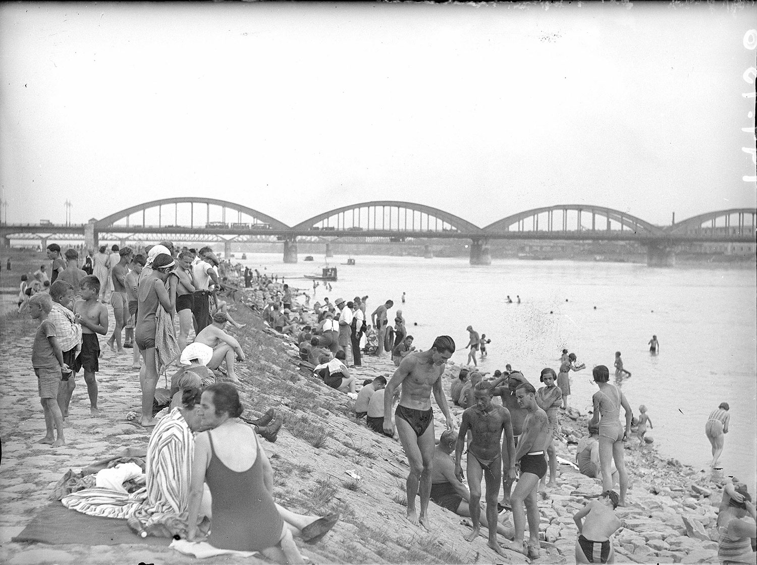 Viele Badende auf dem Ufer, im Hintergrund eine Brücke