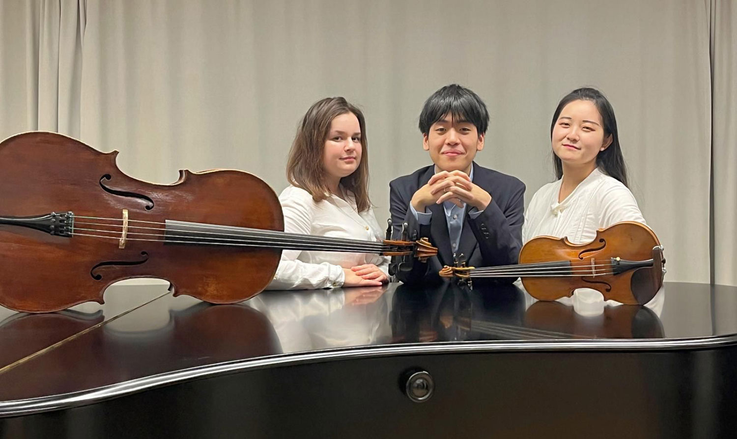 Zwei Musikerinnen und ein Musiker in der Mitte stehen hinter einem Flügel auf dem ein Cello und eine Geige liegen 