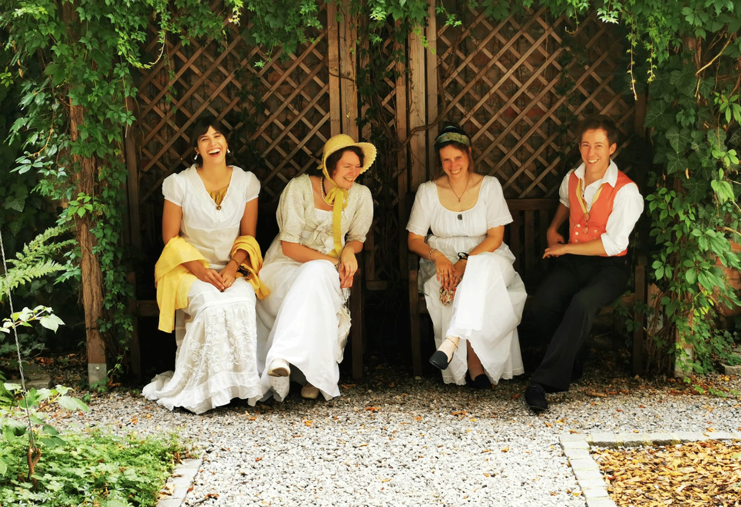 Drei Frauen und ein Mann in historischen Köstumen sitzen auf einer Bank im Graten des Haydnhaus