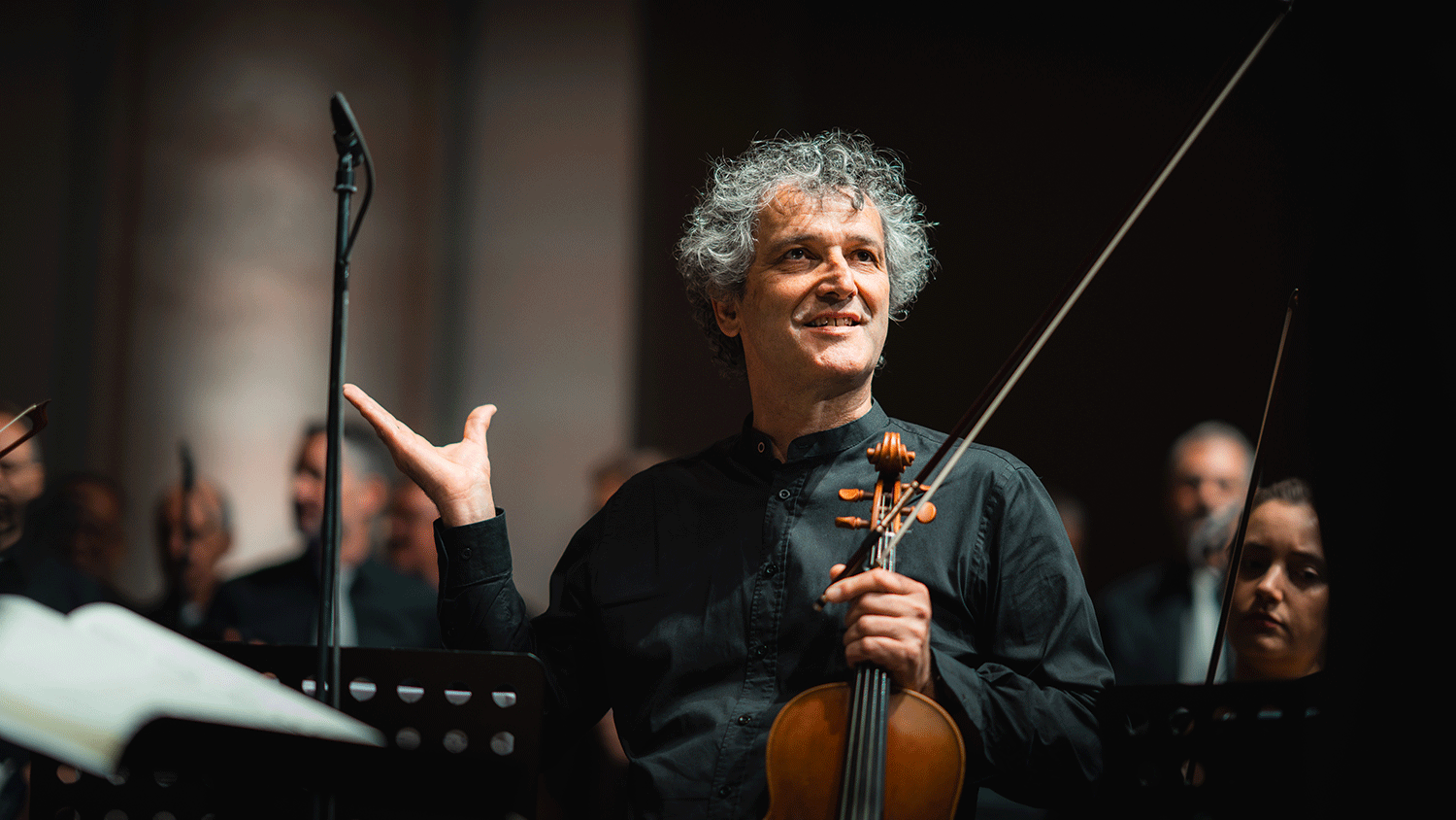 Musiker mit Geige in der Hand steht zwischen dem Orchester