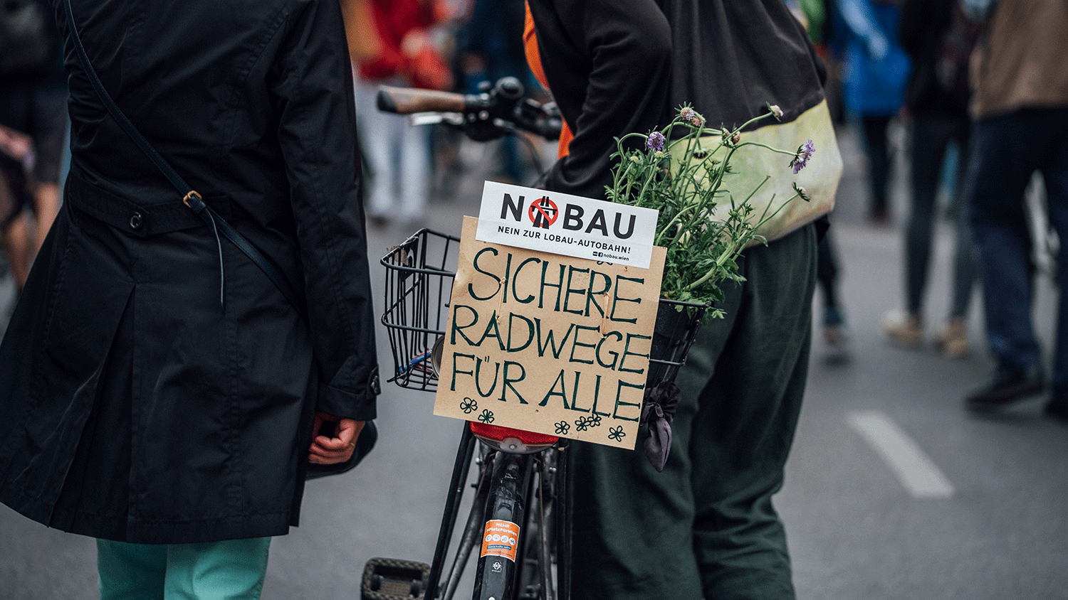 Zwei Personen von hinten schieben ein Fahrrad mit einem Schild mit der Aufschrift 