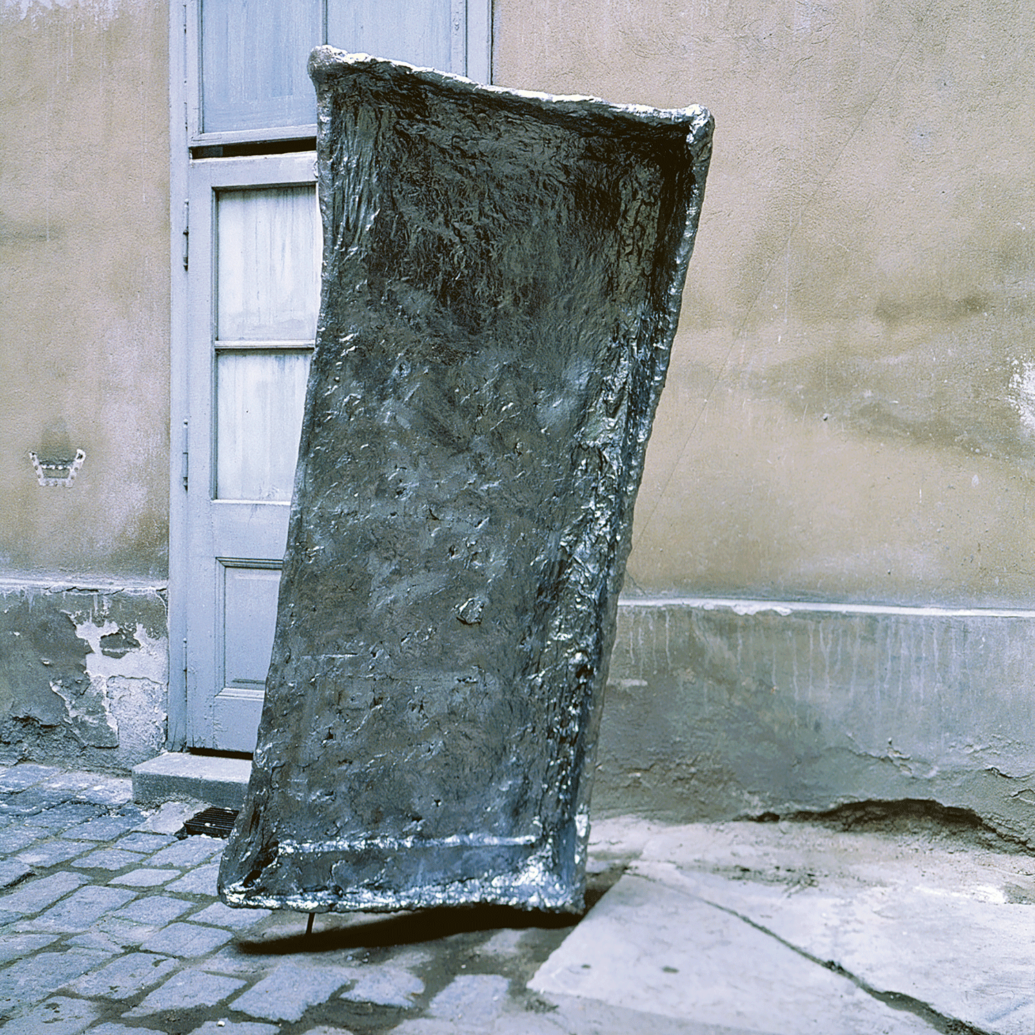 Rechteckige Skulptur vor einer Hausmauer mit Tür